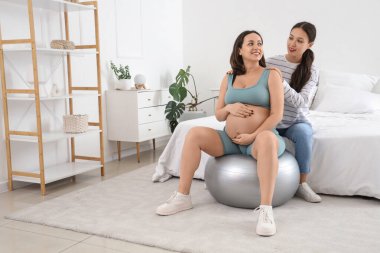 Hamile bir kadının yatak odasında spor eğitimi aldığı genç Asyalı doğum koçu.
