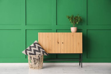 Küçük zeytin ağacı ve yeşil duvarın yanındaki yastıklı ahşap dolap.