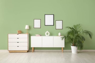 Oturma odasındaki yeşil duvardaki boş fotoğraf çerçeveleri.