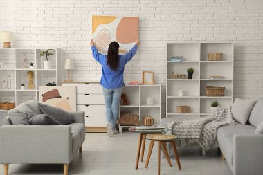 Odadaki beyaz duvara resim asan genç bir kadın.