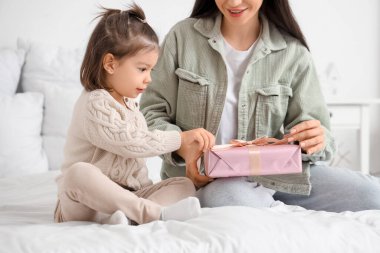 Hediye kutusu olan genç bir anne ve küçük kızı yatak odasında oturuyor.