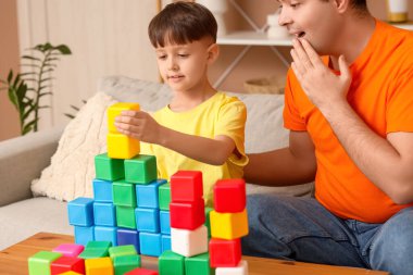 Küçük çocuk ve babası evdeki masada küplerle oynuyorlar.