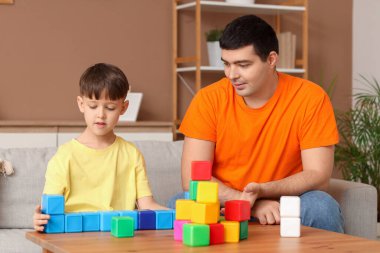 Küçük çocuk ve babası evdeki masada küplerle oynuyorlar.