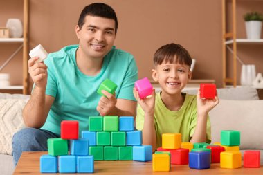 Küçük çocuk ve babası evde renkli küplerle oynuyorlar.