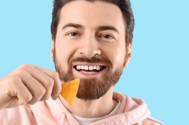 Adam mavi arka planda lezzetli nacho yiyor.