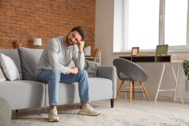 Evdeki kanepede oturan endişeli adam.