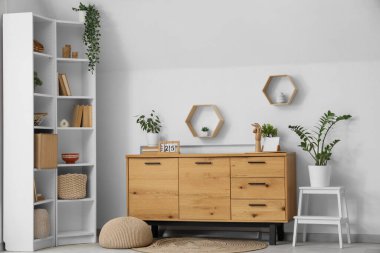 Odanın içinde ahşap tuvalet, raf ünitesi ve bitkiler var.