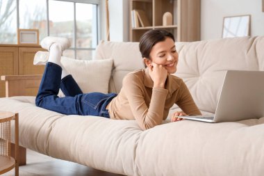 Evdeki kanepede dizüstü bilgisayarı olan genç kız.