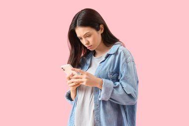 Pembe arka planda cep telefonu olan endişeli genç bir kadının portresi