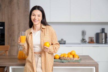 Mutfakta portakal suyu içen genç bir kadın.