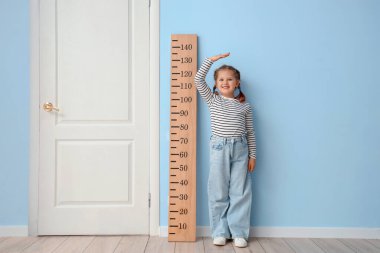 Evdeki mavi duvarın yanında küçük bir kız stadyum ölçer ile boy ölçüyordu.