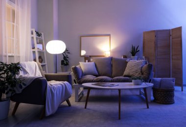 Geceleri koltuğu, kanepesi ve parlak lambaları olan oturma odasının içinde.