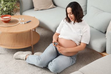 Genç hamile kadın evde glukometre kullanıyor. Gebelik Diyabet Konsepti