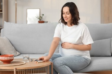 Genç hamile kadın evdeki masadan glukometre alıyor. Gebelik Diyabet Konsepti