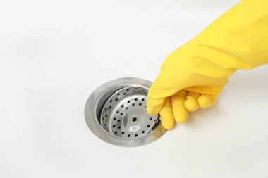 Lastik eldivendeki kadın eli seramik mutfak lavabosuna süzgeç yerleştiriyor, yakın plan.