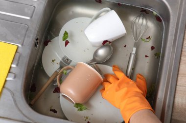 Metalik mutfak lavabosundaki plastik eldivenli kadın tabakları temizliyor.