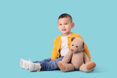 Mavi arka planda oturan oyuncak ayılı şirin Asyalı çocuk.