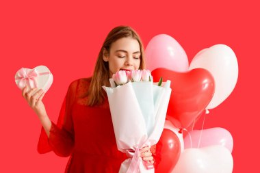 Hediye kutusu, çiçek buketi ve kırmızı arka planda kalp şeklinde balonları olan güzel bir kadın. Sevgililer Günü kutlaması