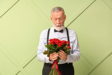 Yeşil arka planda bir buket gülle şoke olmuş olgun bir adam. Sevgililer Günü kutlaması