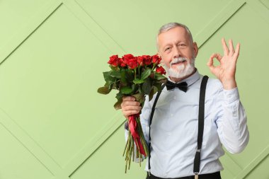 Elinde gül buketi olan olgun bir adam yeşil arka planda iyi görünüyor. Sevgililer Günü kutlaması