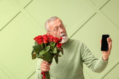 Yeşil arka planda gül buketi ve cep telefonu olan olgun bir adam. Sevgililer Günü kutlaması