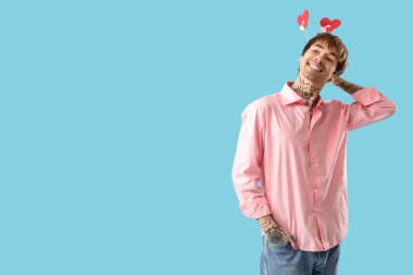 Funny young man with paper hearts on blue background. Valentine's day celebration