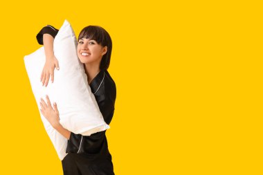 Sarı arka planda yumuşak yastıklı pijamalı mutlu genç kadın.