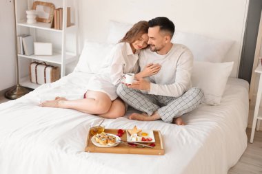 Sevgililer Günü 'nde yatakta kahvaltı eden genç çifte sarılmak.