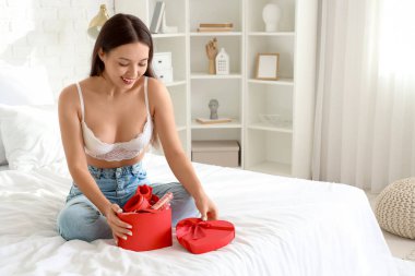 Yatak odasında hediye kutusuyla seks oyuncakları taşıyan genç Asyalı kadın. Sevgililer Günü kutlaması