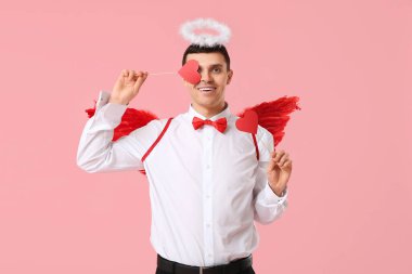 Aşk tanrısı gibi giyinmiş, pembe arka planda kağıt kalpli genç bir adam. Sevgililer Günü kutlaması