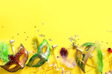 Mardi Gras için sarı arka planda parti kornaları ve dekorları olan karnaval maskeleri.