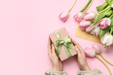 Hediye kutusu olan kadın eller, bir buket güzel lale ve pembe arka planda bir zarf. Uluslararası Kadınlar Günü