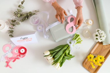 Hediye kutusu olan kadın elleri, paketleme malzemeleri ve arka planda güzel çiçekler. Uluslararası Kadınlar Günü
