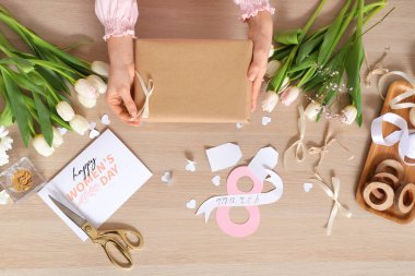 Hediye kutusu olan kadın elleri, güzel çiçekler, tebrik kartı ve tahta arka planda paketleme malzemeleri. Uluslararası Kadınlar Günü