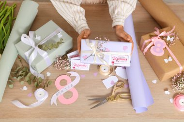 Güzel hediye kutuları ve tahta arka planda paketleme malzemeleri olan kadın elleri. Uluslararası Kadınlar Günü
