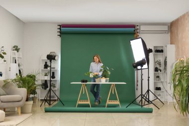 Fotoğraf stüdyosundaki yeşil arka planda bitkileri olan kadın fotoğrafçı.