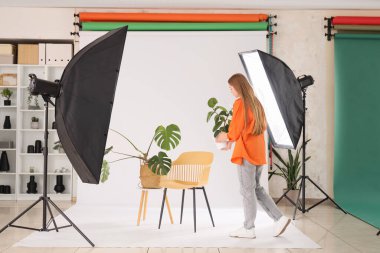 Genç bayan fotoğrafçı, ev bitkileriyle fotoğraf stüdyosunda çekim hazırlığı yapıyor.