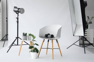 Modern stüdyoda çiçekli sandalye, fotoğraf makinesi ve ışıklandırma ekipmanı.