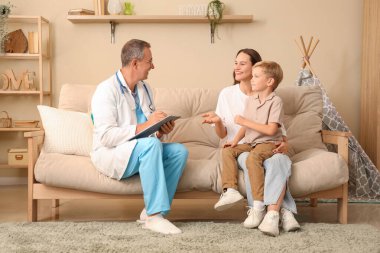 Erkek çocuk doktoru evde küçük bir çocuk ve annesiyle çalışıyor.