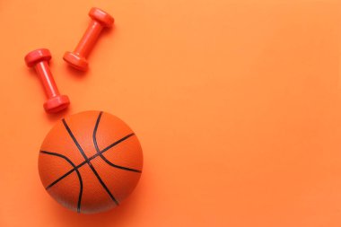 Turuncu arka planda dambıllarla basketbol oynamak için top