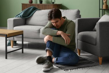 Depresyondaki genç adam evde yerde oturuyor.