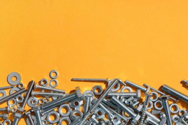 Turuncu arka planda farklı cıvatalar, vidalar ve krom fındıklar var.