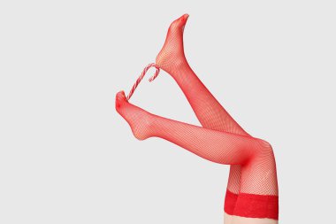 Gri arka planda şeker kamışı olan kırmızı çoraplı genç kadın bacakları. Noel kutlaması