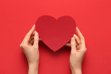 Renkli arka planda kırmızı kağıt kalpli bir kadın eli. Sevgililer Günü kutlaması