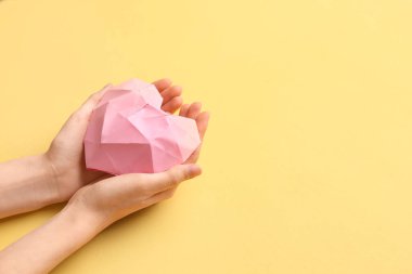 Sarı arka plandaki kağıttan yapılmış pembe kalpli kadın elleri. Sevgililer Günü kutlaması