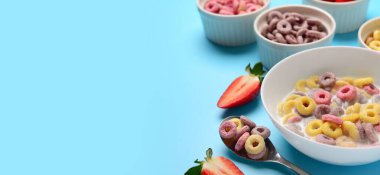 Süt ve çilekli farklı tatlı mısır gevreği halkaları açık mavi arka planda metin için boşluk, yakın çekim