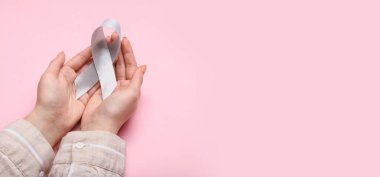 Beyin kanseri farkındalığı kurdelesini elinde tutan kadının elleri pembe arka planda, mesaj için yeri var.