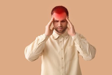 Bej arka planda başı ağrıyan genç bir adam.