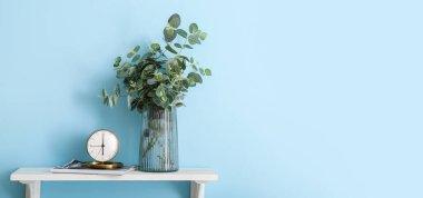 Saat ve vazo, okaliptüs ve dergi, mavi duvarın yanında. Tasarım için pankart