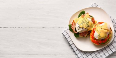 Beyaz ahşap arka planda lezzetli yumurtalı Benedict tabağı, yazı için yer, üst görünüm